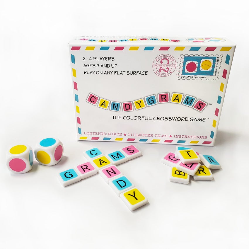Candygrams game. “The colorful crossword game.” The white box looks like a stamped envelope. It has pink, yellow, and blue dashes that border the lid of the box, with a stamp illustration in the top-right. The title in the middle is in alternating colored blocks. In front of the box are 2 large dice with colored dots on each side in pink, yellow, and blue. To the right are letter game tiles spelling out candy, down, and grams, across. To the right of the spelled words is a pile of more colored letter tiles.