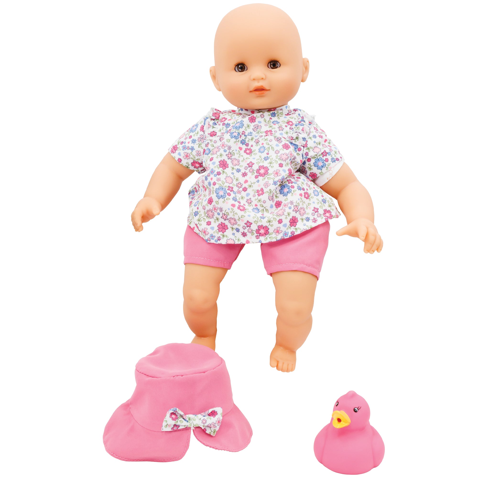 Corolle’s Bebe Coralie. The light skinned baby doll has brown blinkable eyes and is standing. She is wearing pink shorts and a floral shirt with a variety of pinks and periwinkle colored flowers in different sizes. In front, and to the left of the baby, is a pink hat with a bow in the middle that matches the shirt print. To the right of the hat is a pink rubber ducky.