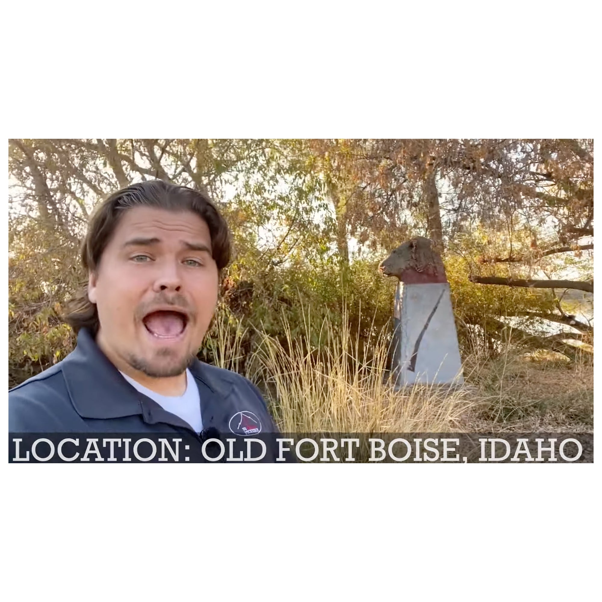 Screen shot of the male host in the middle of speaking. In the background you can see trees and a lion head statue. White text on the bottom of the image reads "Location: Old Fort Boise, Idaho."