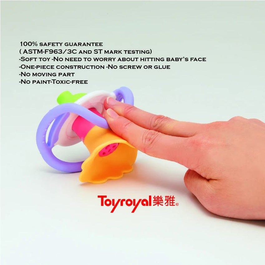 A hand is pushing down on the Flower Whistle to show flexibility. The flower top is dark yellow with a pink center. The round middle portion of the whistle is white in the middle and lavender on the outside. The whistle portion at the bottom is bright green. Text on the image reads 100% safety guarantee, soft toy, 1 piece construction, no paint, toxic free.