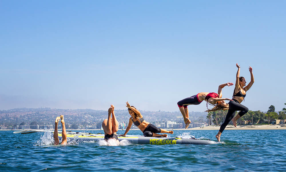 5 women jumping off large paddle board