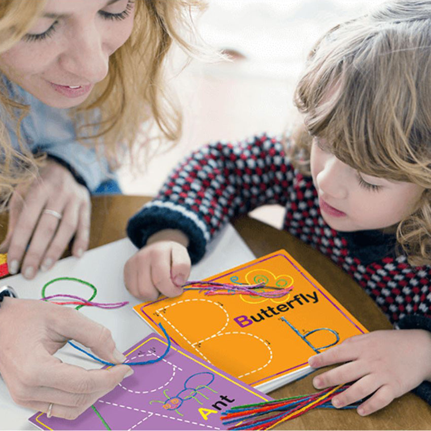A mom and daughter are sitting at a round table playing with the Wikki Stix Alphabet set. The are working on the letters A and B. The purple A card has an ant and the upper and lowercase letter A on it. The orange B card has a butterfly with an upper and lowercase b on it. There are wax sticks in many colors on top of the table.