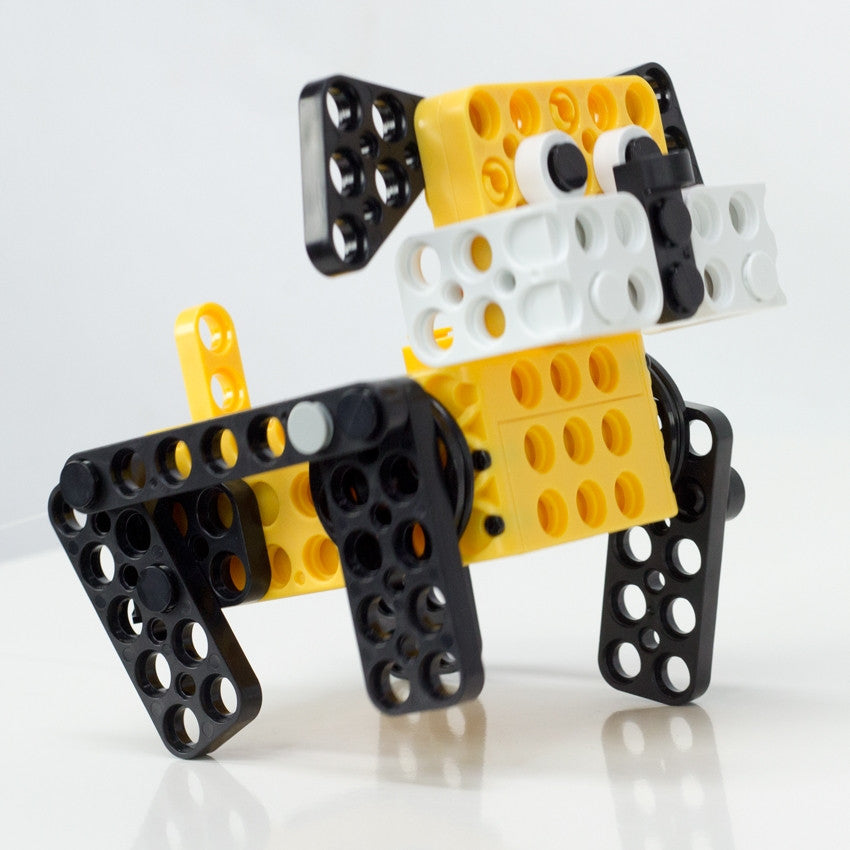 Robotis Play 600 Pet dog robot in the process of walking. Dog face and body are yellow and the legs, eyes, nose, and ears are black with some white accents.