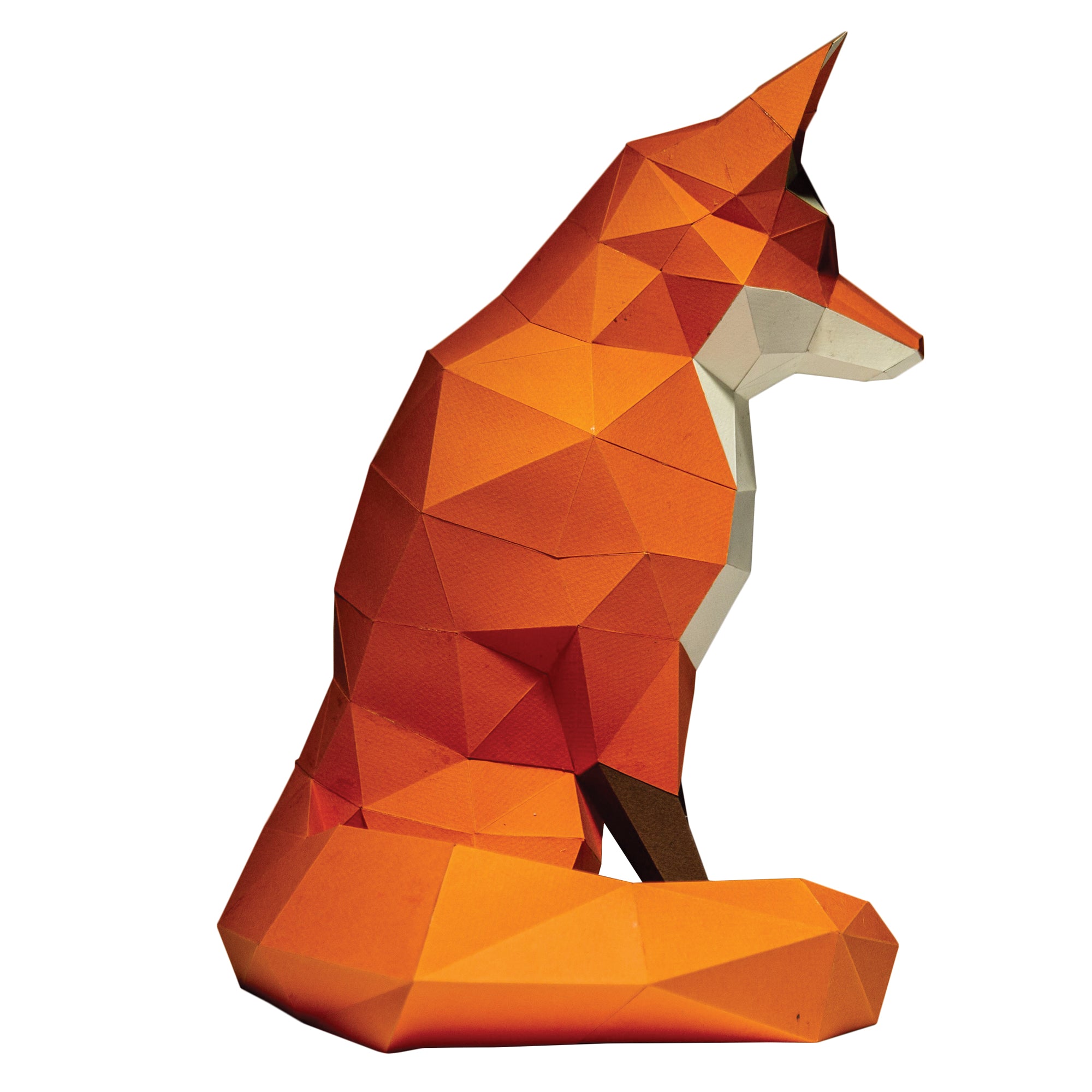 Side view of a Papercraft fox on a white background. Geometrical-shaped fox that is folded and cut paper pieces glued together. Fox is mainly a dark orange with black paws and a white chest and chin area.