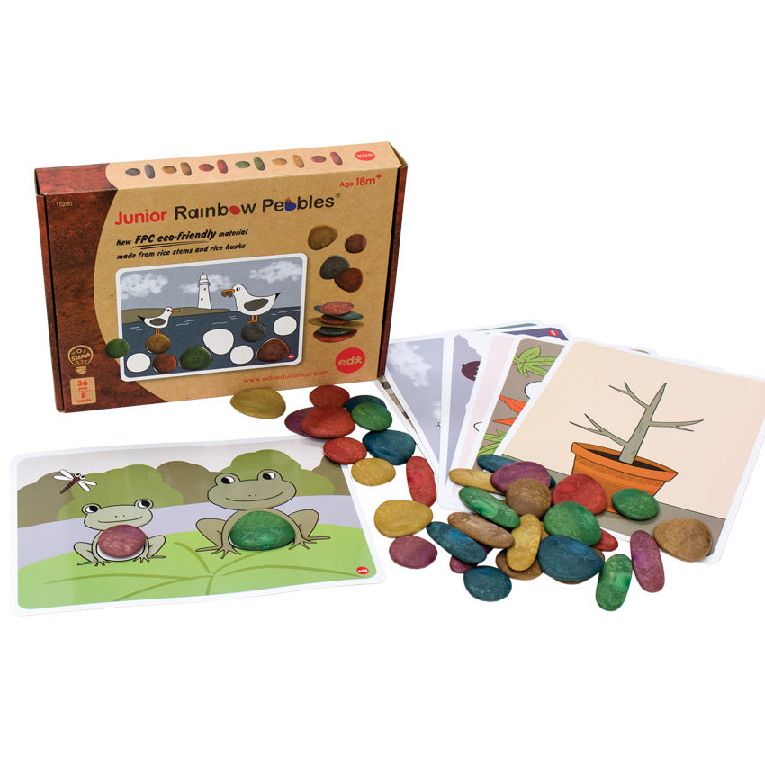 Junior Rainbow Pebbles, Earth Tones, box with contents spread out over a white surface. The activity cards have illustrations with blank spaces to put the pebbles. Visible cards are 1 with 2 frogs on a lily pad and 1 of a stem in a planter pot. There are more cards stacked below the visible ones. There are pebbles, in many shapes and colors, spread over the surface and cards.