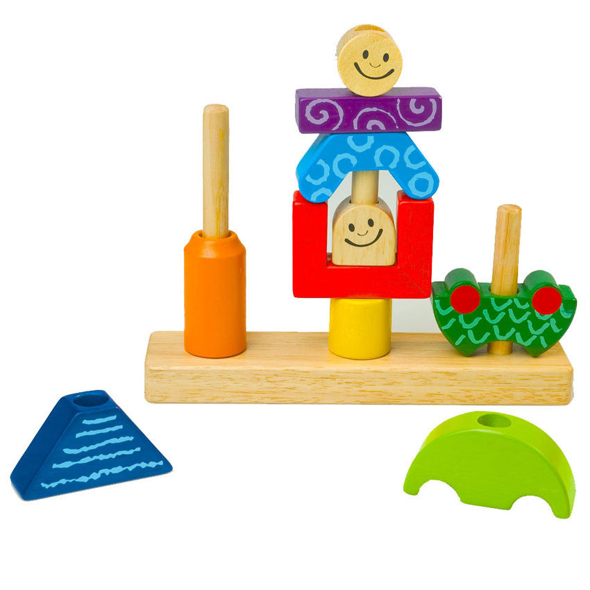 Day & Night game in play. The wooden game has 3 large pegs with pieces placed over the pegs. The first peg has a tall rounded orange piece. The second peg has a rounded yellow piece on bottom, then a squared red piece on top with a smiling face inside, then a blue triangle-type shape, then a purple rectangle, then a smiling face piece on top. The third peg has a bottom green half round piece. There is a blue triangle and half round green piece off to the side.
