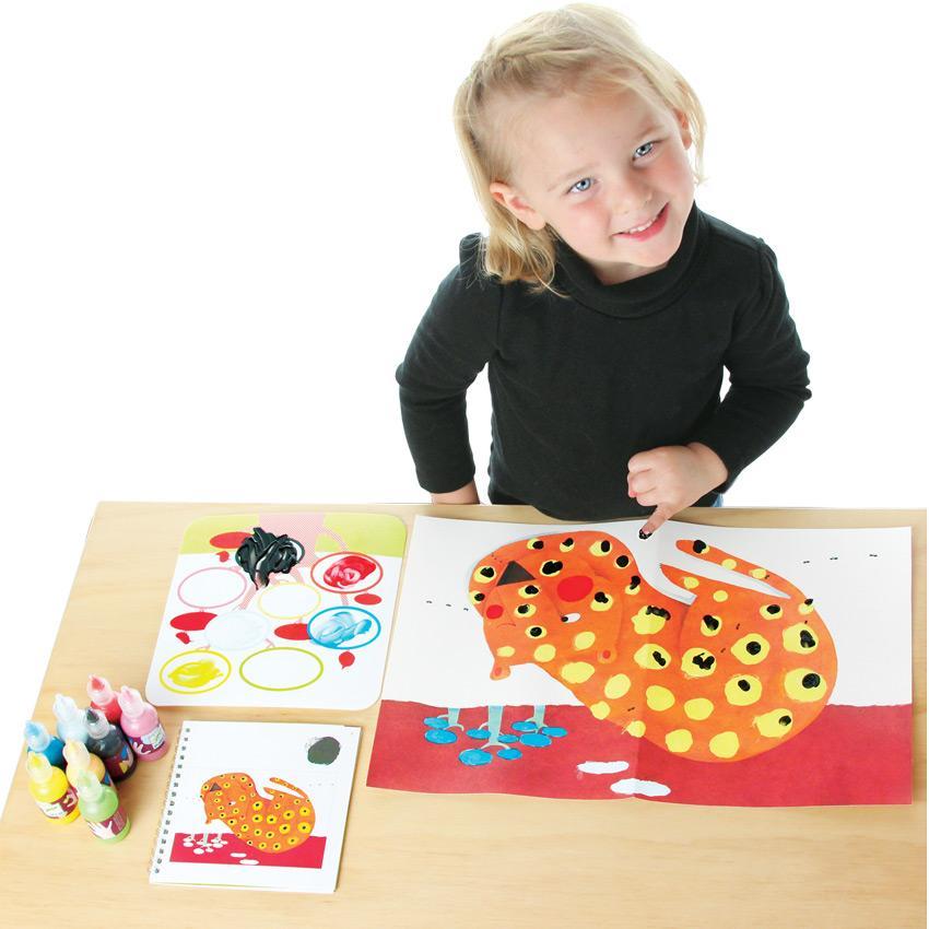 A young blonde girl working on the Djeco Finger Tracks leopard project. She smiling with her head tilted and is painting black spots on the leopard with her left pinky finger. On the table in front of her is the leopard project. To the left is a paint pallet  with splotches of paint and above is the instruction book open to a leopard page and 8 paint bottles.