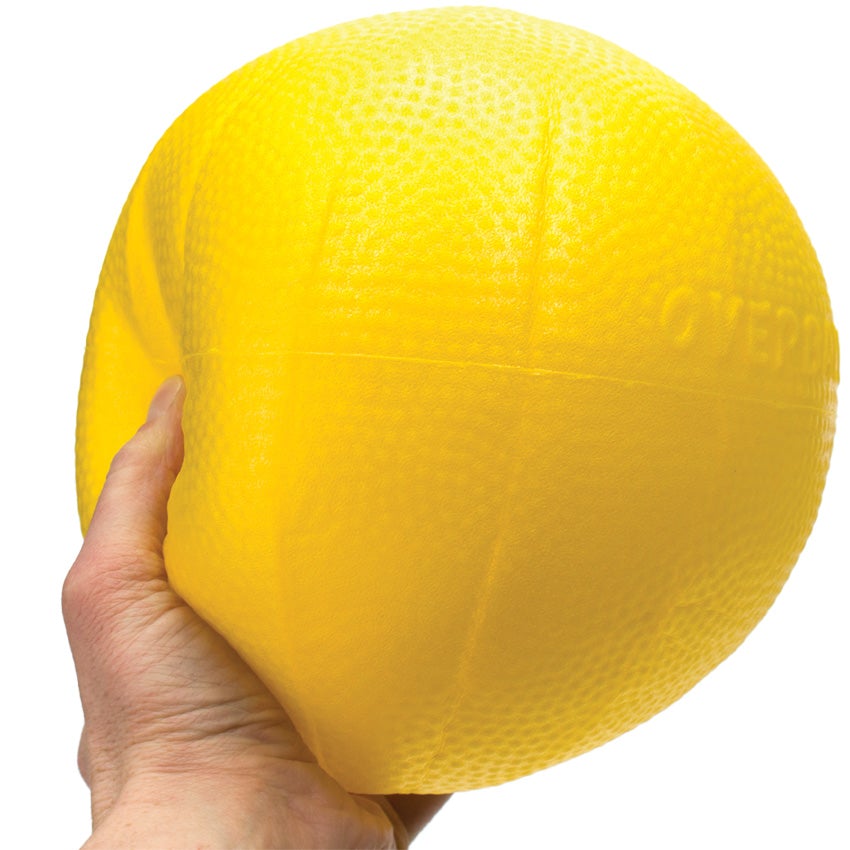 Gymnic Over Ball in yellow being gripped by a hand to show the ball can be flexible for easy catching. The ball has a slight bumpy texture. The words over ball are embossed on the ball.