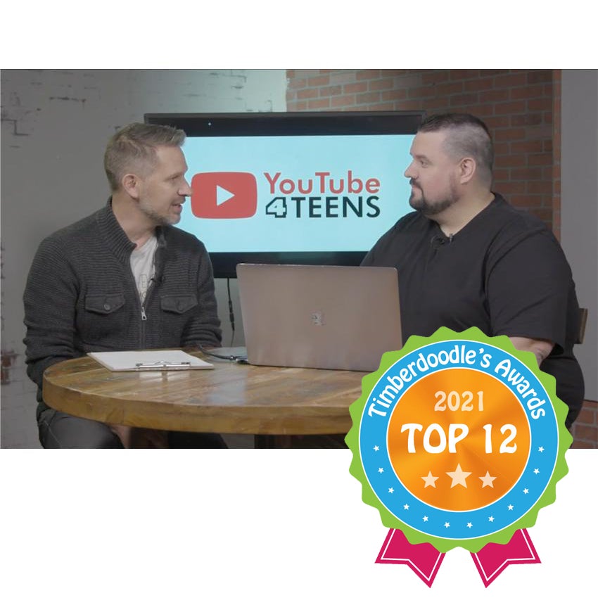 2 men sit at a round wood table looking at each other. There is a clipboard and a laptop on the table in front of the men and a TV with the YouTube 4 Teens logo showing behind them. The man on the left has light grayish colored hair and is wearing a dark gray jacket and dark colored jeans. The man on the right has a black t-shirt and khaki's. Over the right-bottom of the picture is a "Top 12 Timberdoodle Award."