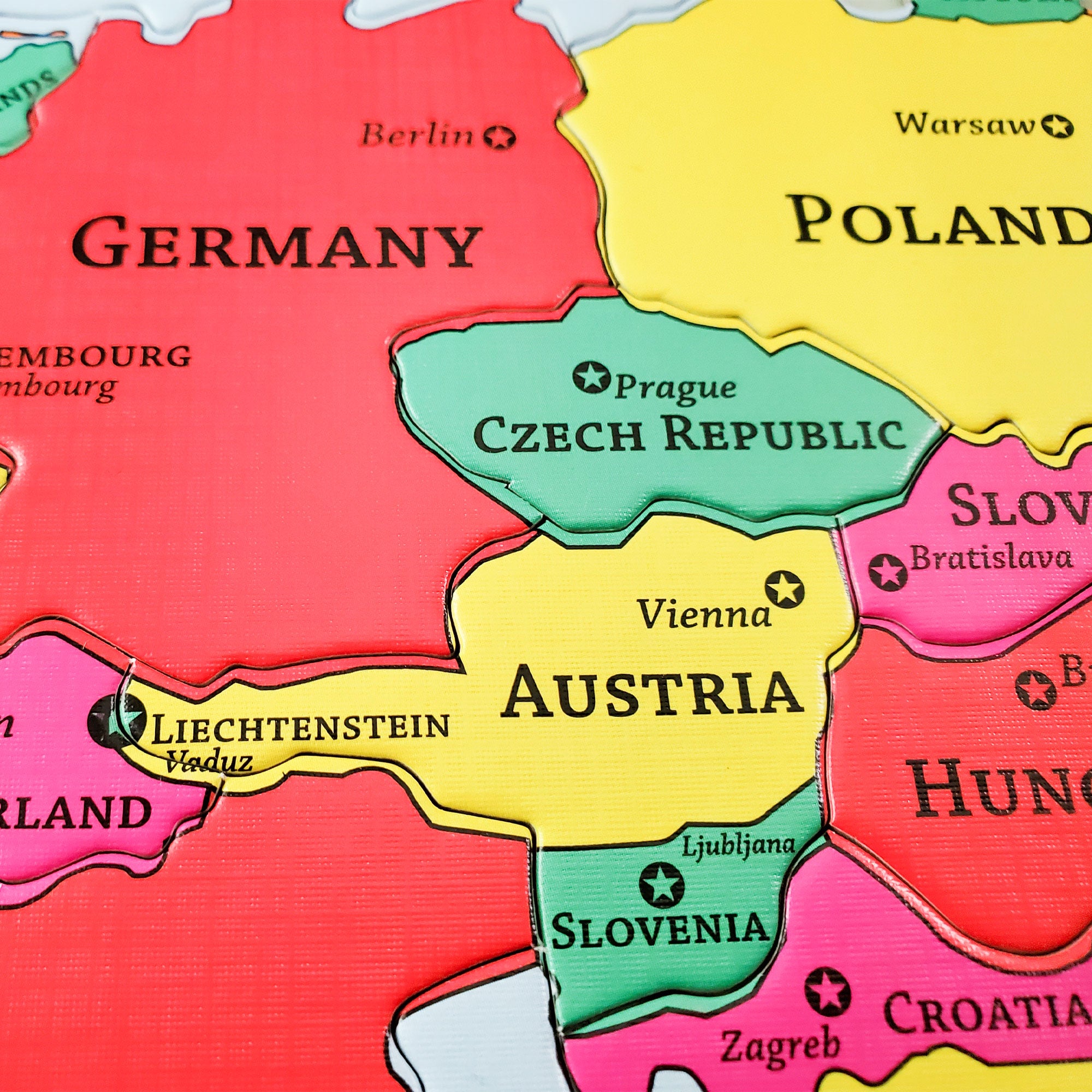 Close up of the Europe Geo Puzzle. The put-together pieces show Germany, Czech Republic, Austria, Slovenia, Poland, Croatia, and the edges of several nearby countries. It also shows the name of each countries' capitol, along with the name of each country. Each country is a different color. The colors are red, yellow, green, and pink.