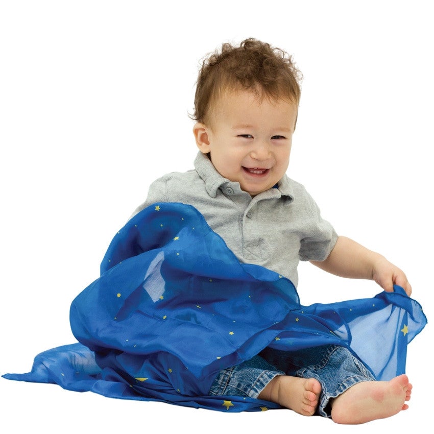Smiling baby pauses from playing peek-a-boo with his starry night playsilk.