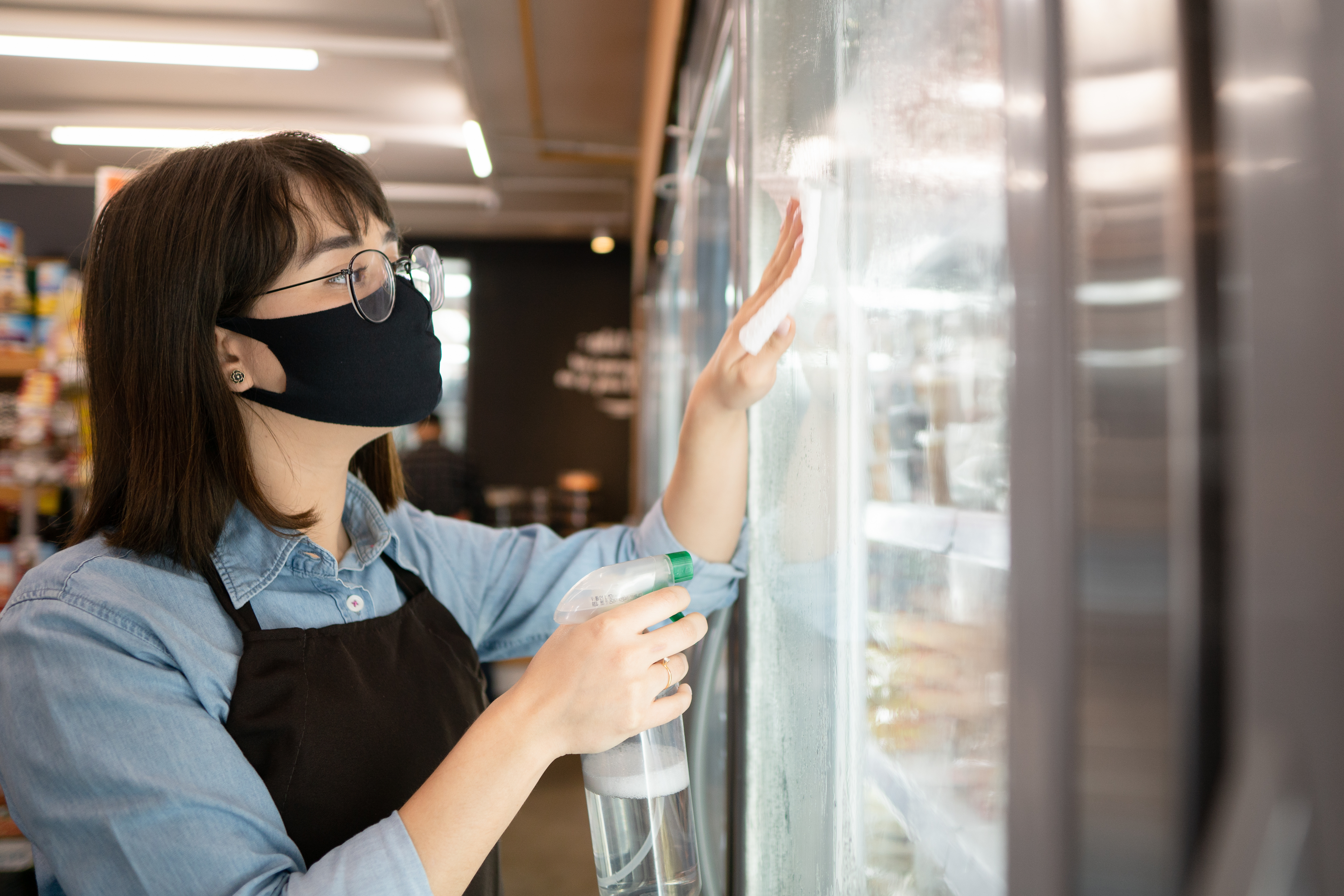 Cleaning staff spraying and wiping glass on fridge section