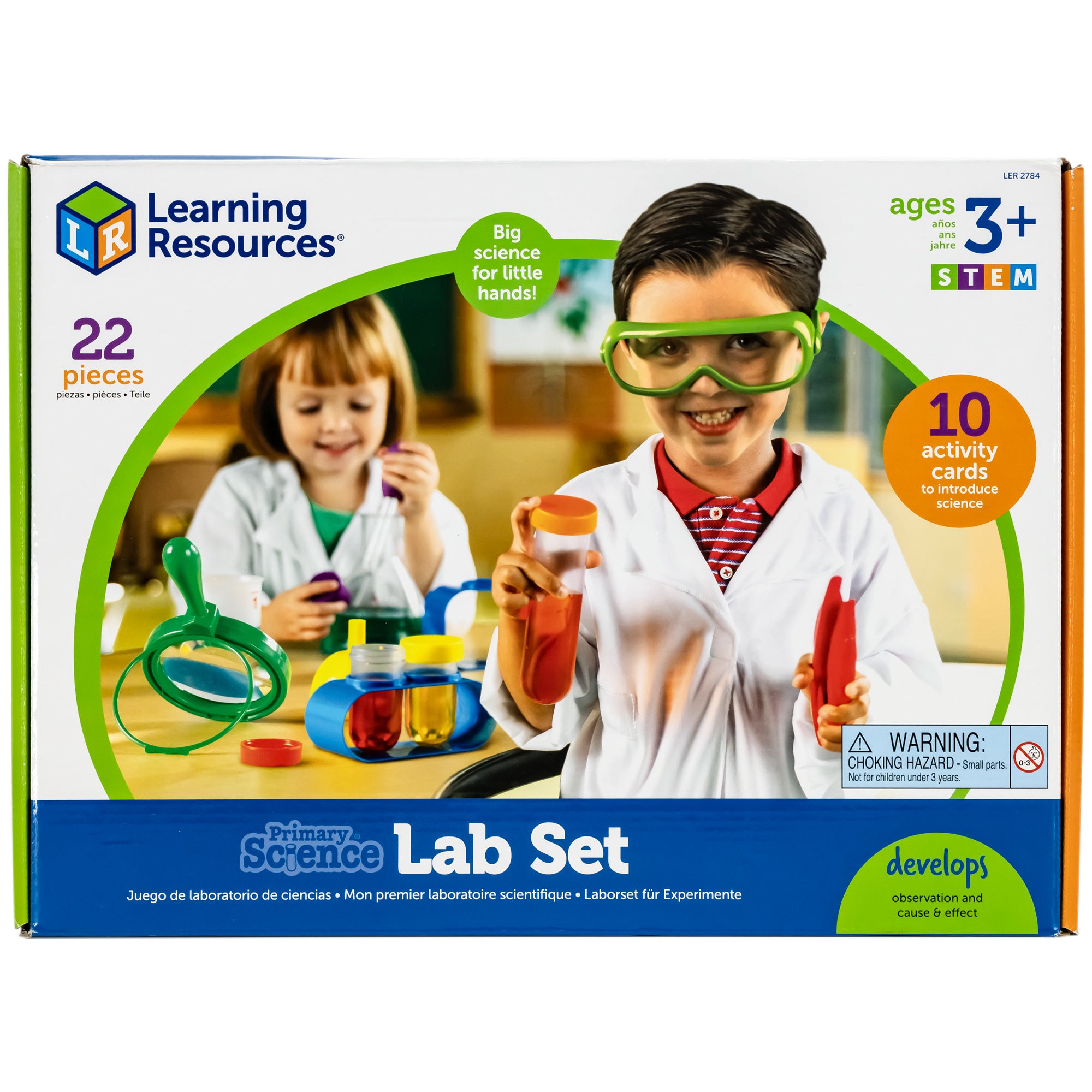 Primary Science Lab Set box cover. Center picture shows 2 children using the lab set items. The boy in the front is holding a test tube with orange liquid and an orange lid in his right hand. He is holding red large tweezers in his right hand and green safety glasses with a white lab coat over a red striped shirt. Behind him is a table with science tools laid out with a girl playing with a beaker and green liquid. She is also wearing a lab coat over a green shirt. 22 pieces with 10 activity cards.