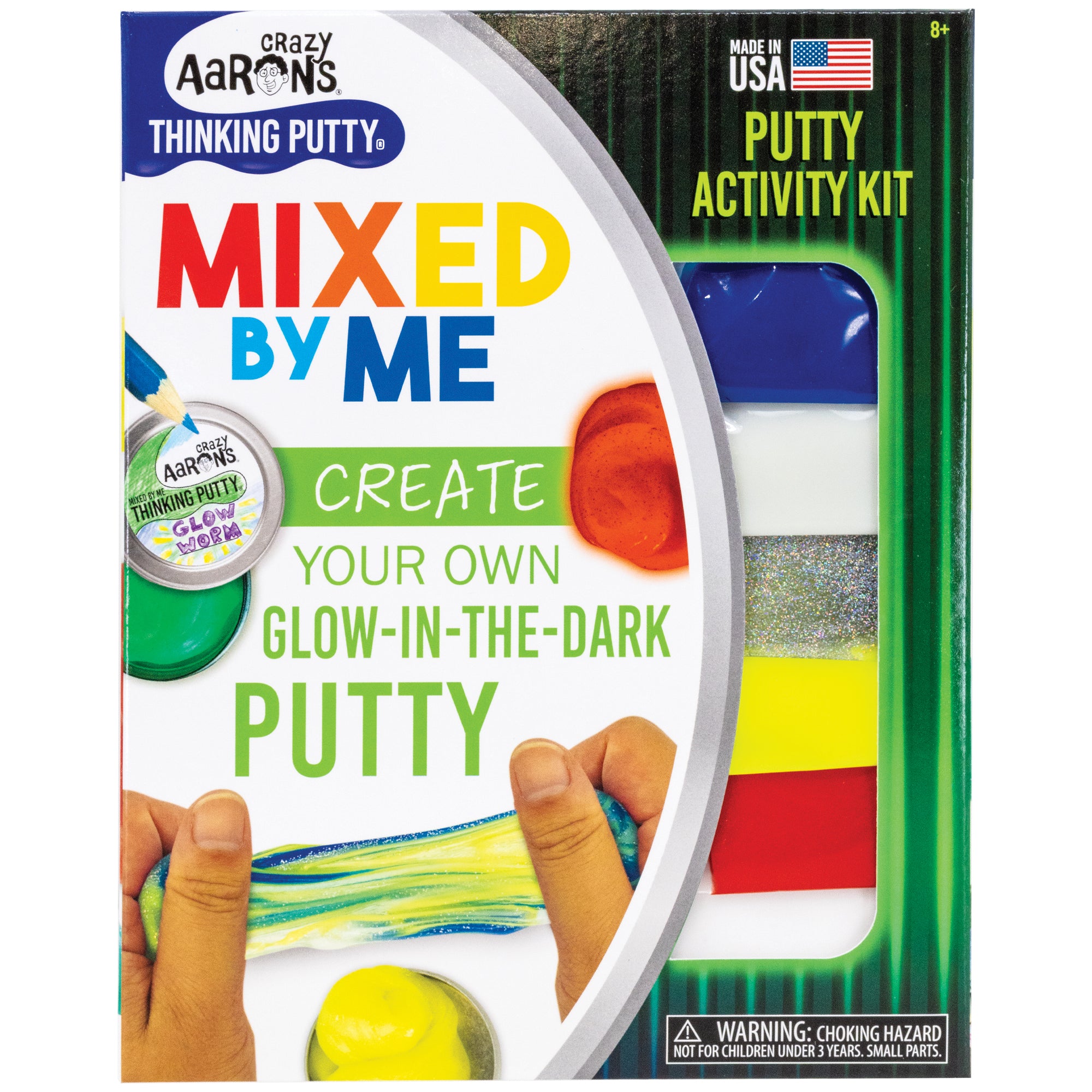 Mixed by Me, Glow, Thinking Putty Kit box cover. The white, black, and green box shows images on the left, including; a green putty in a small tin with a pencil drawing on the lid label, a brick red glob, a yellow glob, and a hand stretching and mixing yellow, blue, and silver glitter together. To the right of the box is a window, showing contents of the kit. The clear, flat, plastic bags contain blue, white, glitter, yellow, and red putty.