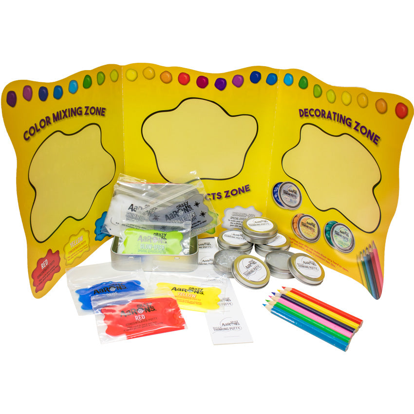 Mixed by Me, Glow, Thinking Putty Kit contents. There is a large, tri-fold, yellow pamphlet standing in the background. Each page shows a large squiggly circle in the middle with tips for creation. On the left is a mint-style tin with small rectangular plastic bags falling out. The plastic bags contain concentrated putty, including blue, red, yellow, white, glitter, and glow. In the middle is a strip of lid labels. To the right are 5 small round tins of clear putty and a set of colored pencils.