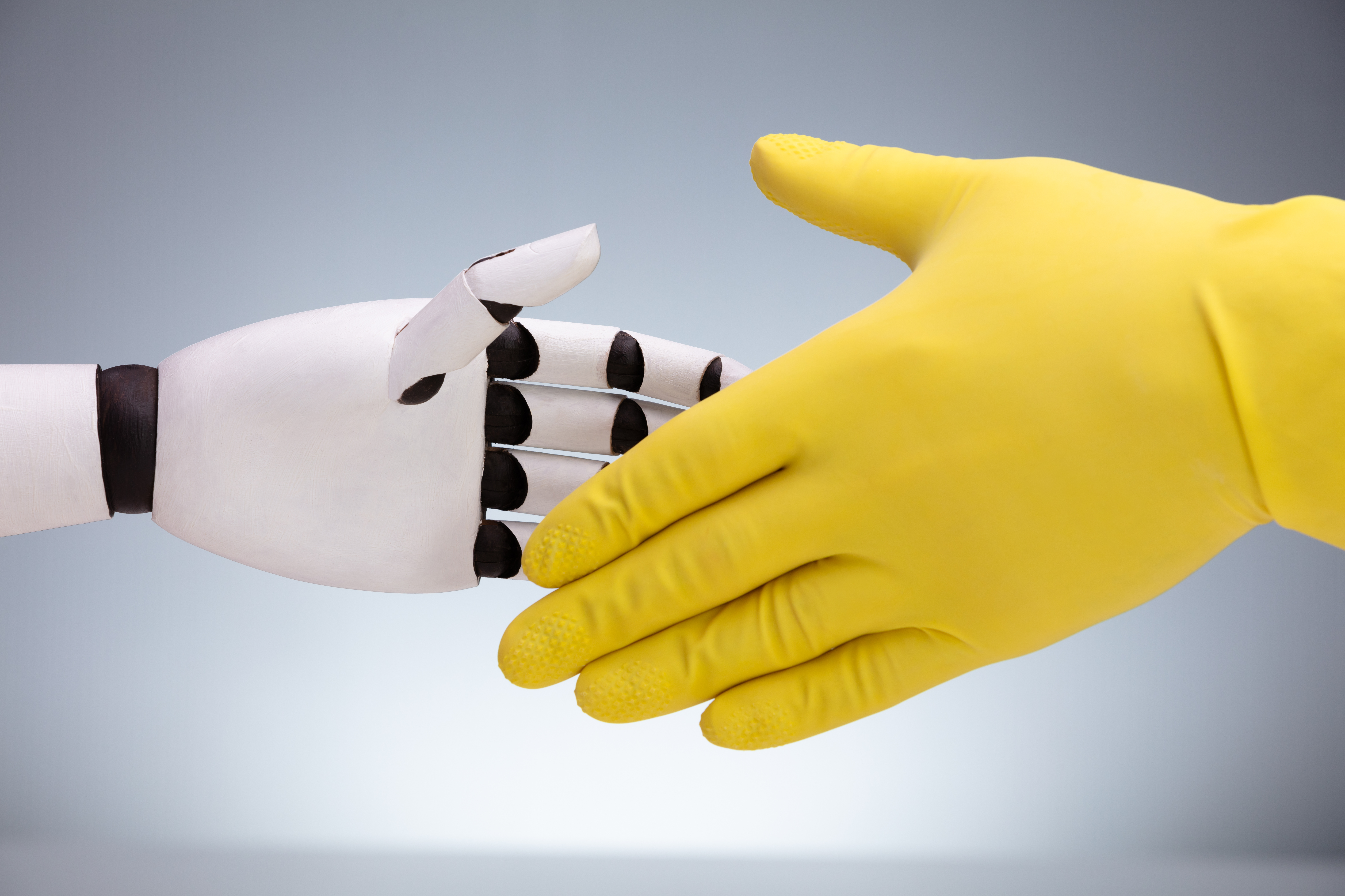 yellow rubber gloved hand shaking a robot hand 