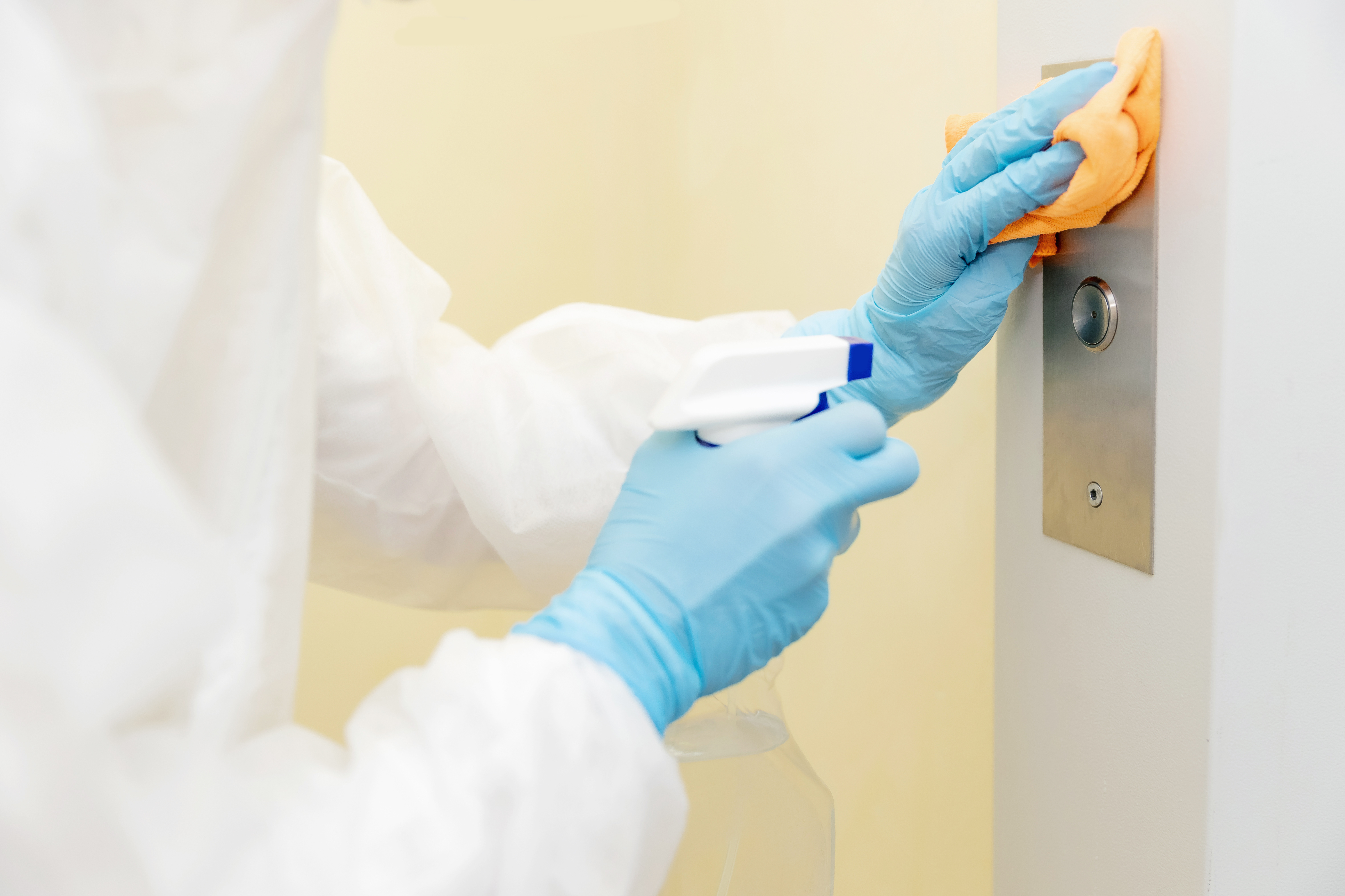 hospital cleaning staff with blue gloves and white protective clothing cleaning high touch elevator buttons