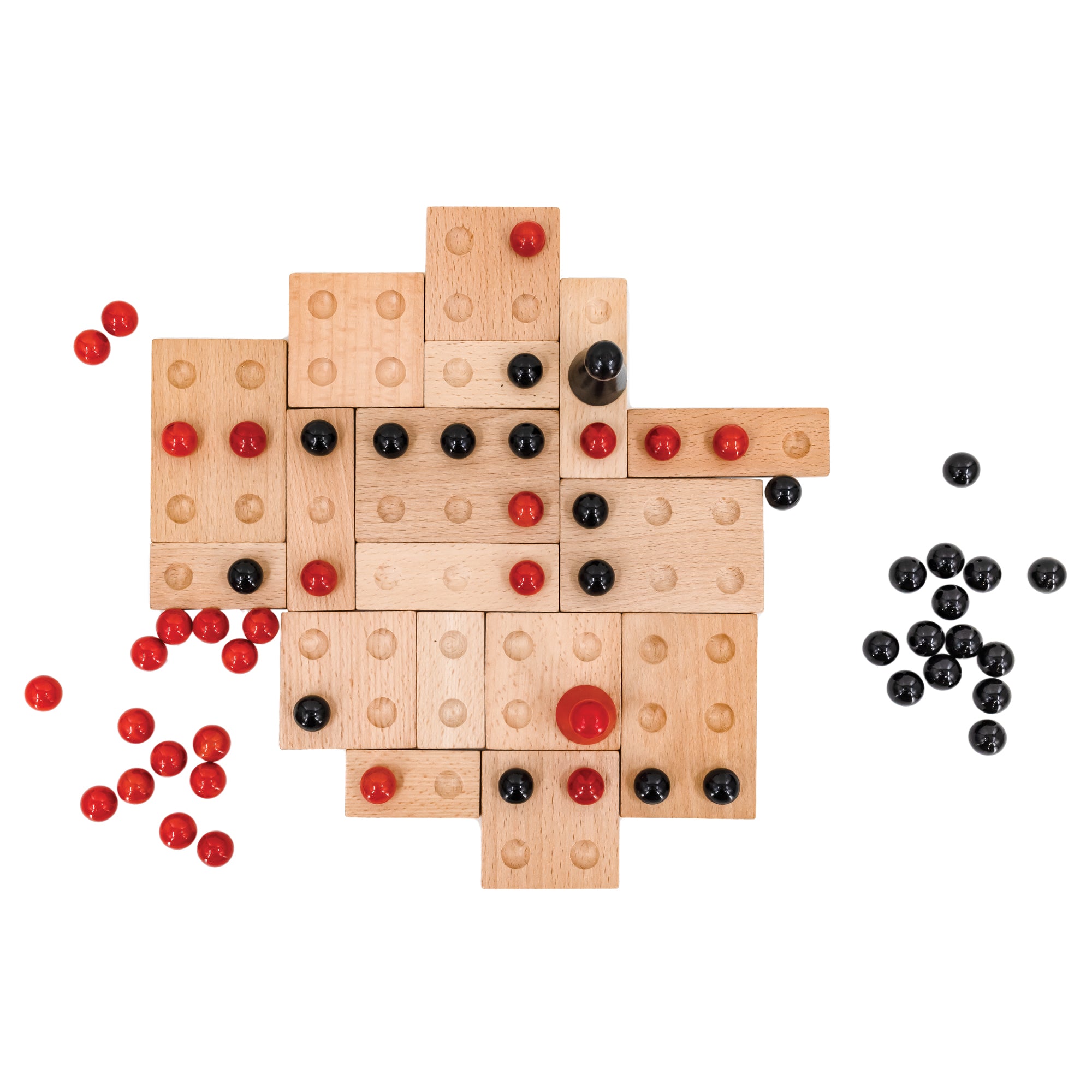 Top view of the Kulami game in play. There are many square and rectangle wood pieces with divots to place black and red marbles. The wood pieces are placed randomly against each other for form a gapless board. The marbles are randomly placed on top with 2, larger, cone-shaped pieces with a rounded top in the middle; 1 red, and 1 black. There is a pile of black marbles off to the right of the board and a pile of red marbles off to the left of the board.