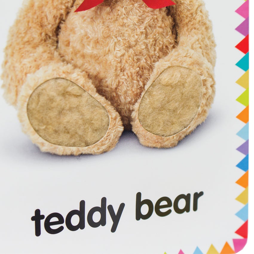 My First Touch and Feel Cards: First Words card showing a close up of a teddy bears feet. You can see fuzzy cotton on the feet, providing real texture. The text “teddy bear” is written below the bear. The background is white and there are colored triangle-shaped flags all around the border.