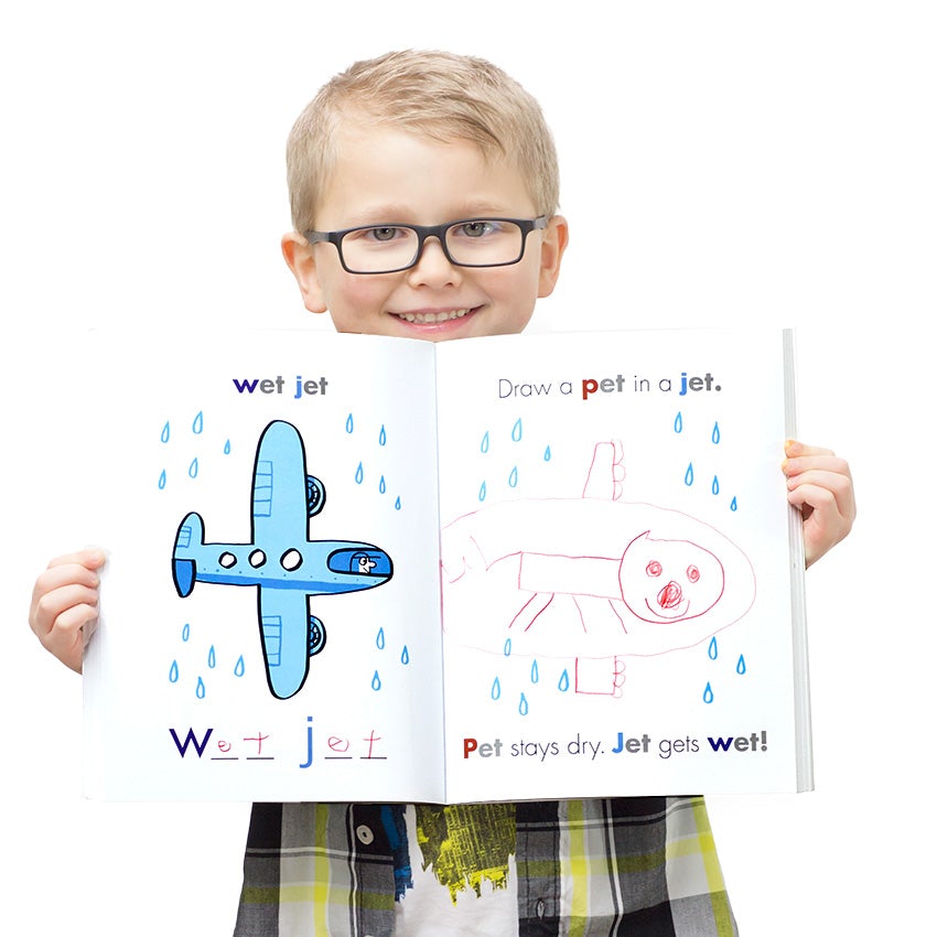 A young blonde boy in glasses and a plaid shirt holding the I Can Doodle Rhymes open. The left page  shows a blue jet flying in the rain. The text reads "wet jet." The right page reads "draw a pet in a jet." The child has doodled a red smiling animal  inside a red jet with rain drops surrounding. Under the doodle reads "Pet stays dry. Jet gets wet."