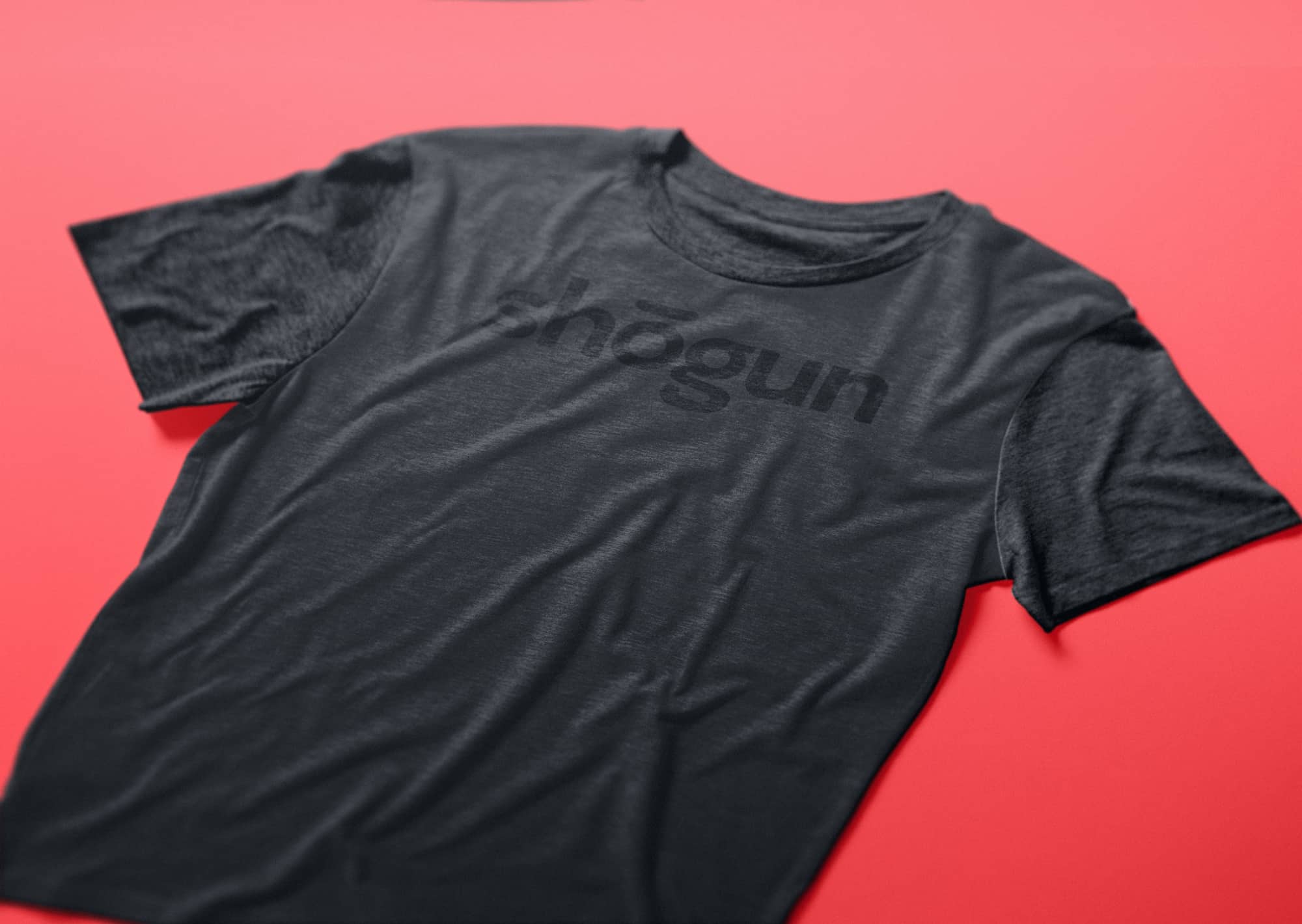 A black t-shirt with a black Shogun logo on it. The t-shirt is on a red surface.