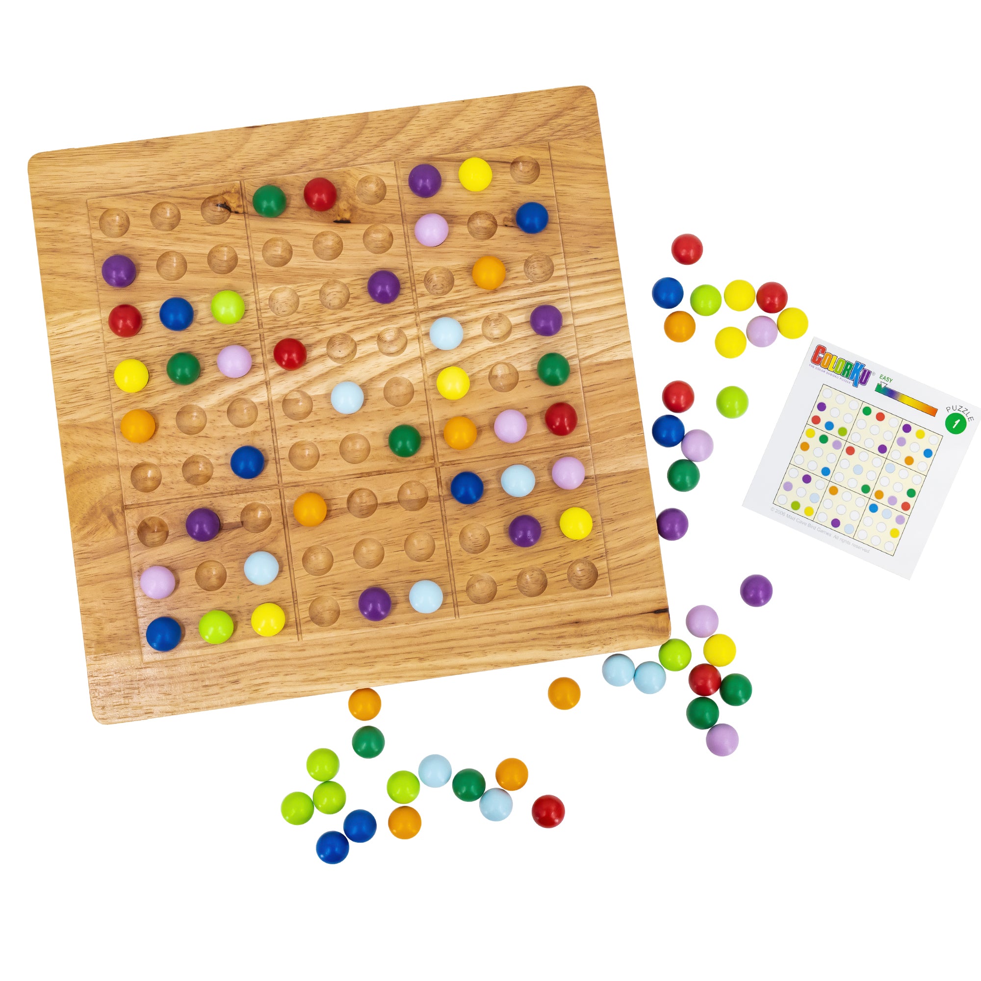 A layout of the ColorKu board and game pieces. The large wooden board has many ball pieces in place. To the right is a challenge card. All around the board are scattered ball pieces. The colored ball pieces are red, orange, yellow, bright green, dark green, light blue, dark blue, light purple, and dark purple.