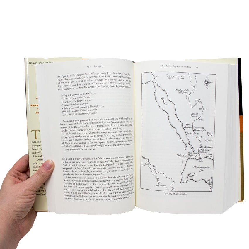 A hand on the left is holding The History of the Ancient World book open to show inside pages. The left page shows paragraphs of text. The right page shows a map of The Middle Kingdom, including the Red and Mediterranean Seas.
