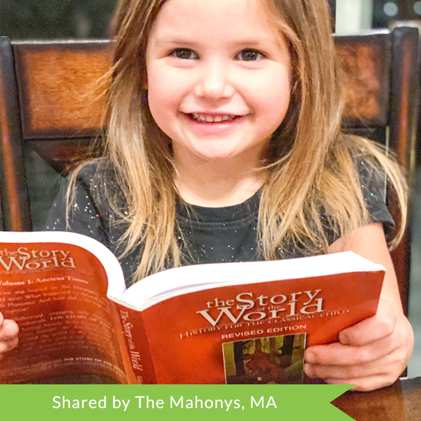 A customer photo of a smiling, dark blonde girl sitting at a table and holding The Story of the World, Volume 1, Ancient Times in her hands. The cover is mainly orange with a small illustration of a wolf with babies in the woods in the center of the cover.