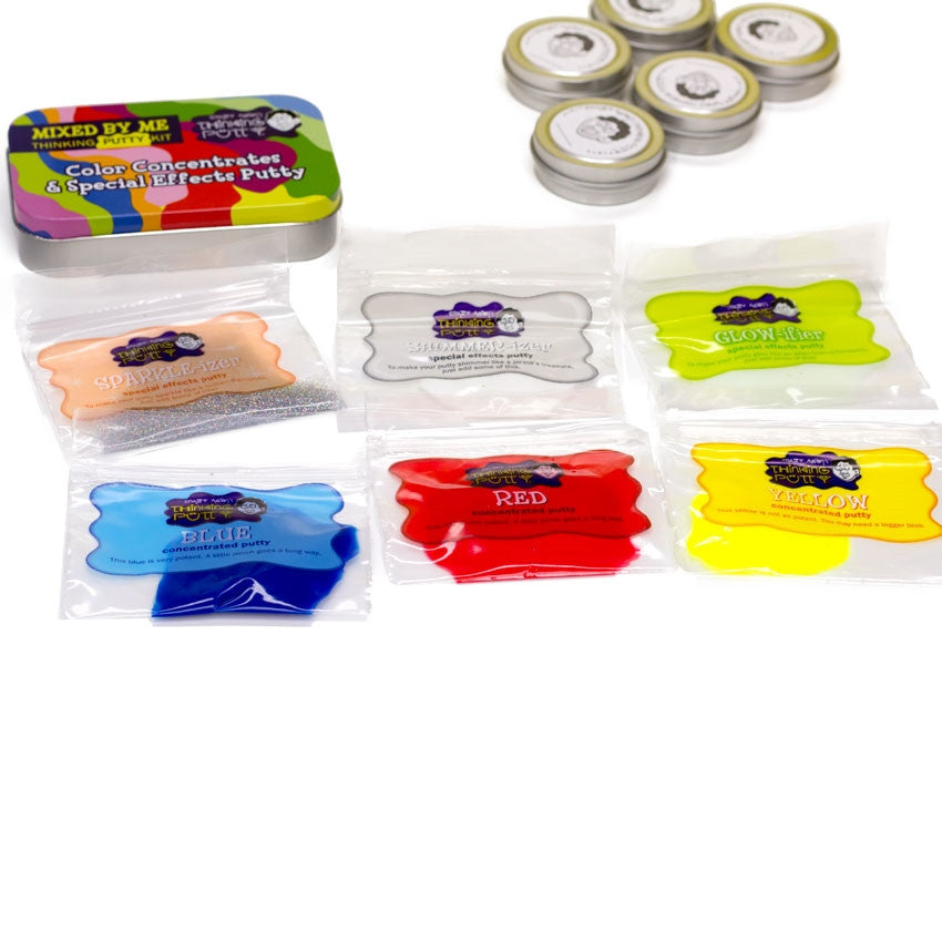 Some of the Mixed by Me, Glow, Thinking Putty Kit contents laid out on a white surface. On the left is a mint-style tin with a colorful lid. To the right are 5 small putty tins with labels placed on top. Below are small rectangular plastic bags laid out in 2 rows of 3. The plastic bags contain concentrated putty, including blue, red, yellow, white, glitter, and glow.