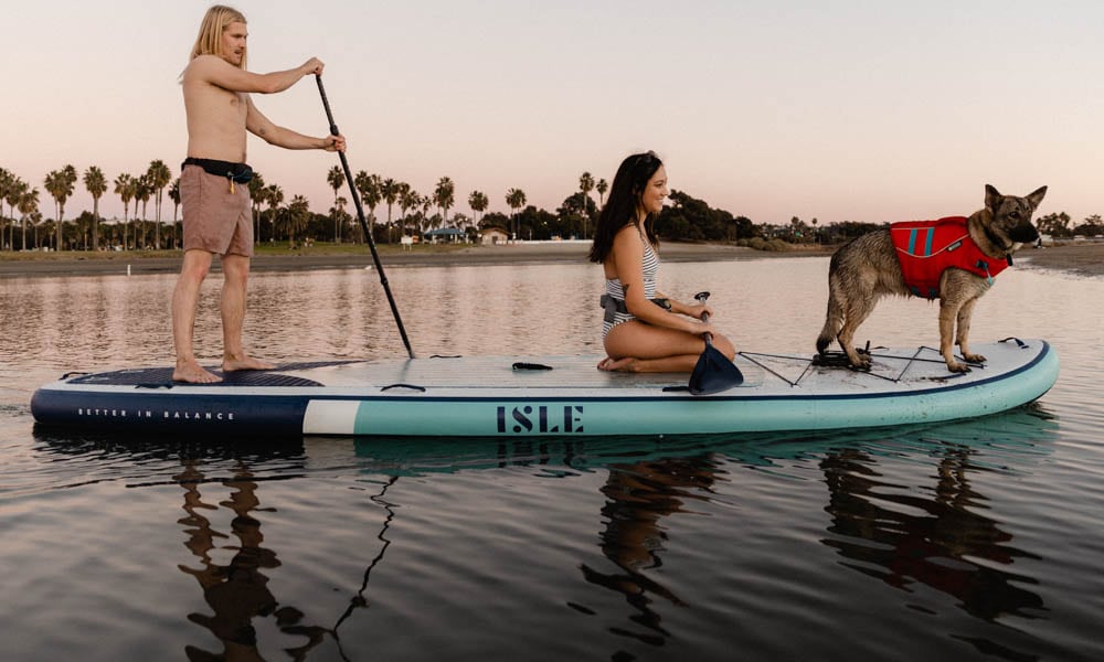 man, woman and dog on large paddle board