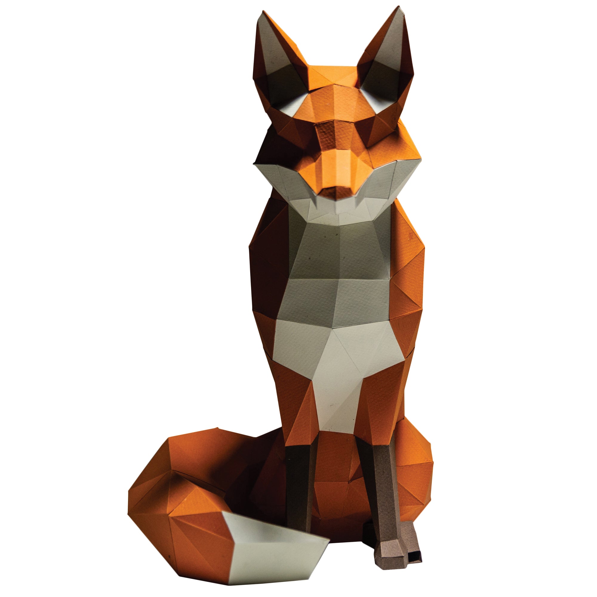 Papercraft fox on a white background. Geometrical-shaped fox that is folded and cut paper pieces glued together. Fox is mainly a dark orange with black paws and a white chest, chin area, inside ears, and tip of tail.