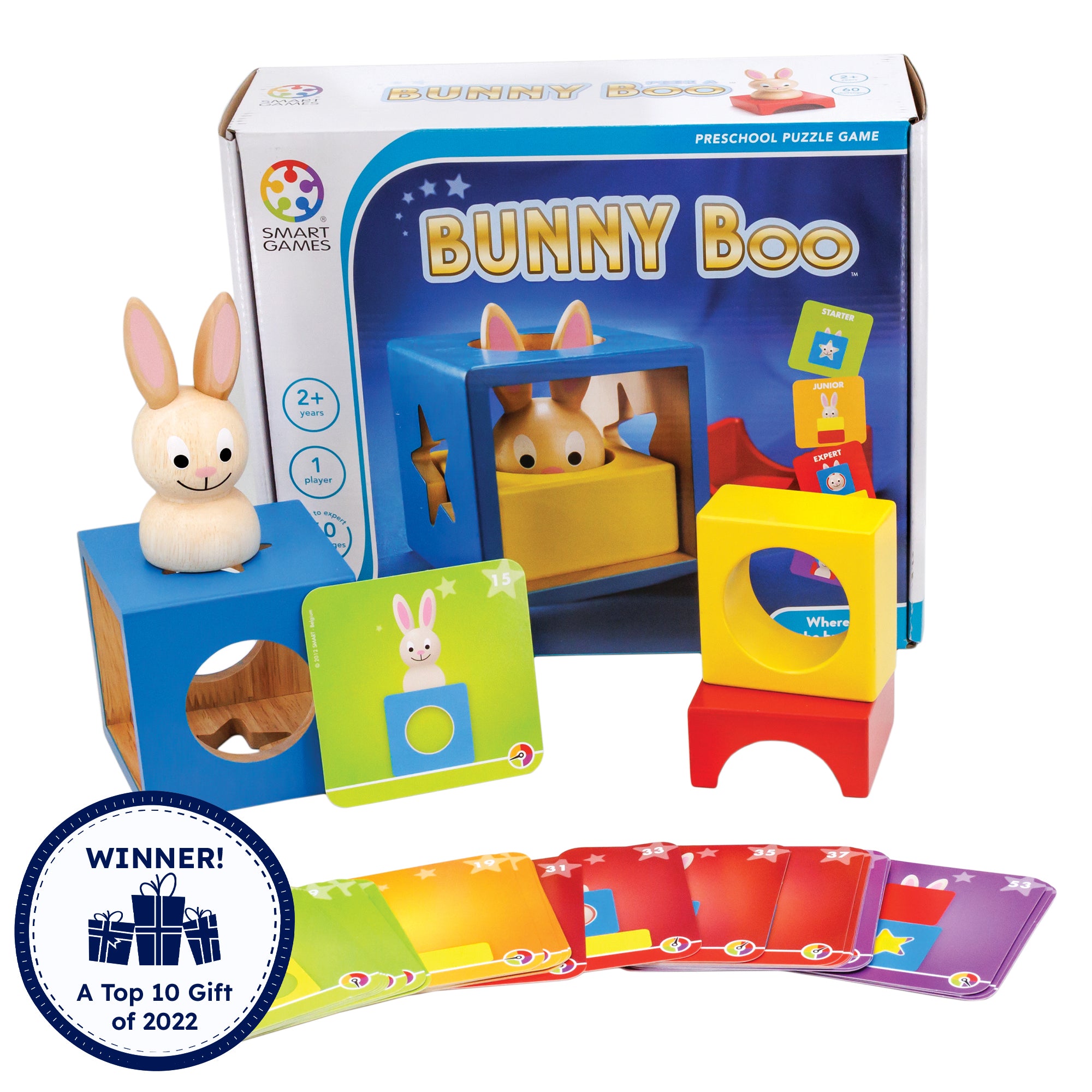 Bunny Boo game box with contents. In front of the box, is a hollow blue wood block with shapes cut out on the sides with a wooden bunny piece on top and a challenge card propped up against it. To the right are a yellow piece with a hollow circle through the middle and a red piece that shows a half circle piece cut out of the middle. There are challenge cards fanned out along the bottom in many colors. There is a badge reading “Winner! A top 10 gift of 2022” in the bottom-left.
